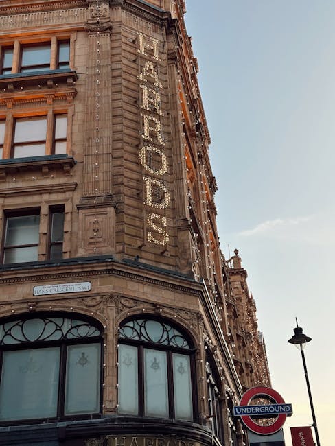A close-up view of a historic building's corner façade in Knightsbridge, featuring ornate stonework and decorative architectural details. The building has a large vertical sign reading 'FEARROD'S' in illuminated letters, positioned on the corner section near the upper floors. The lower part of the building includes tall, arched windows with wood or metal framing, and the windows have decorative elements such as floral motifs. To the right, a traditional streetlamp is visible, along with a London Underground sign indicating proximity to the underground station. The sky above is clear with soft lighting suggesting late afternoon or early evening. The scene reflects the classic city architecture, typically associated with urban environments where private waste collection and rubbish removal services, such as those provided by [COMPANY_NAME], can be employed for maintaining the area’s cleanliness and visual appeal.